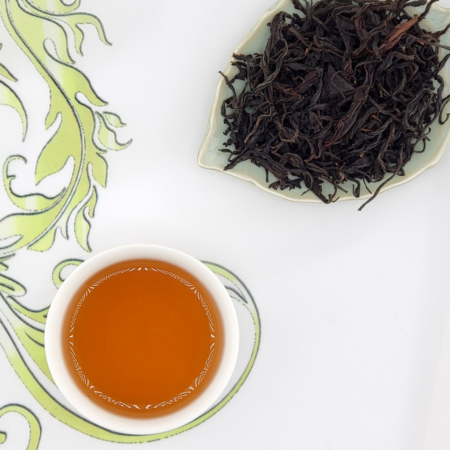 Dried black tea leaves on a leaf-shaped plate with a cup of brewed tea.