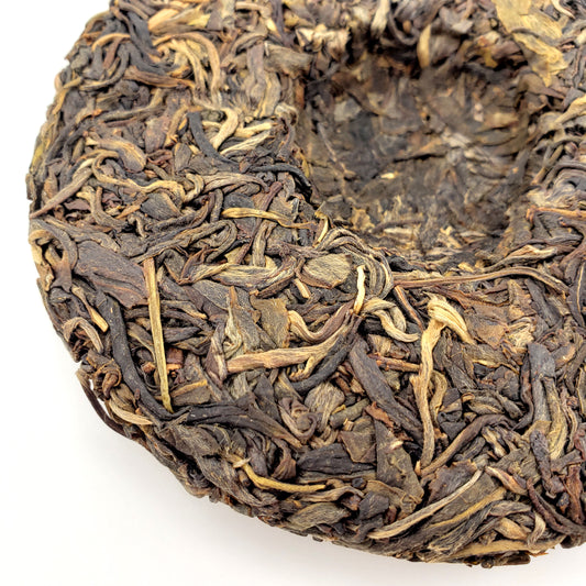 Close-up of a compressed tea cake with dried tea leaves on a white background