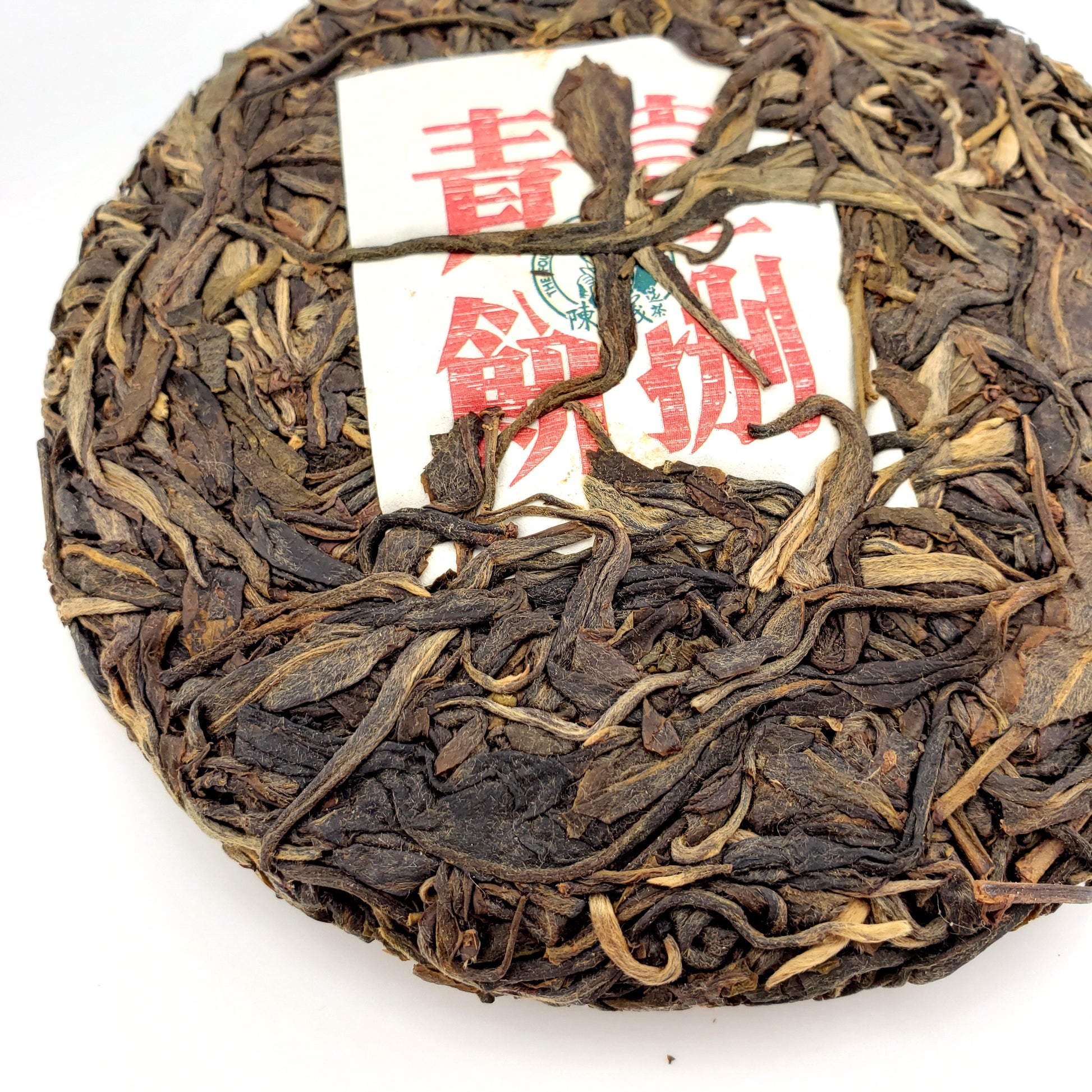 Round cake of compressed tea leaves with a red and white label on a white background