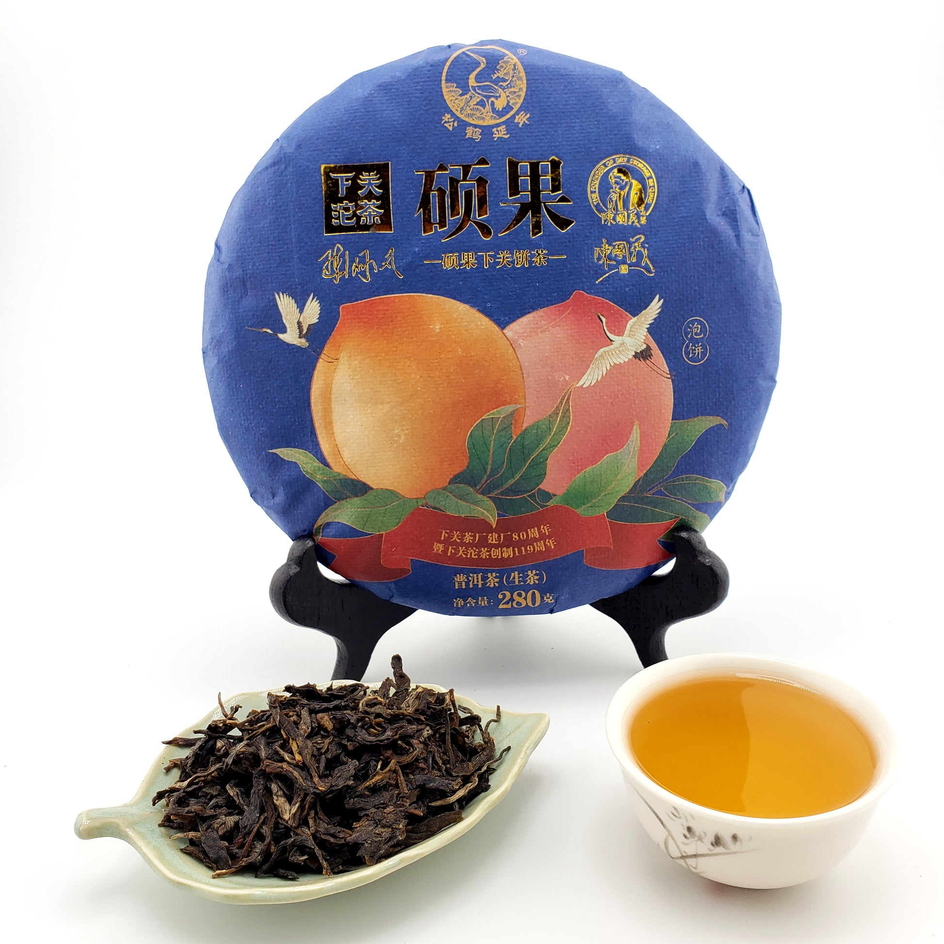 Blue tea cake with peach design, cup of tea, and tea leaves on a white background