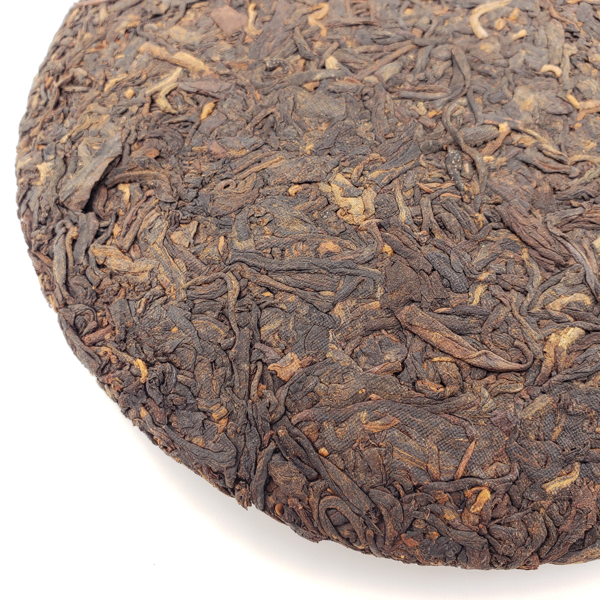 Close-up of a round, pressed tea cake with dark brown leaves on a white background
