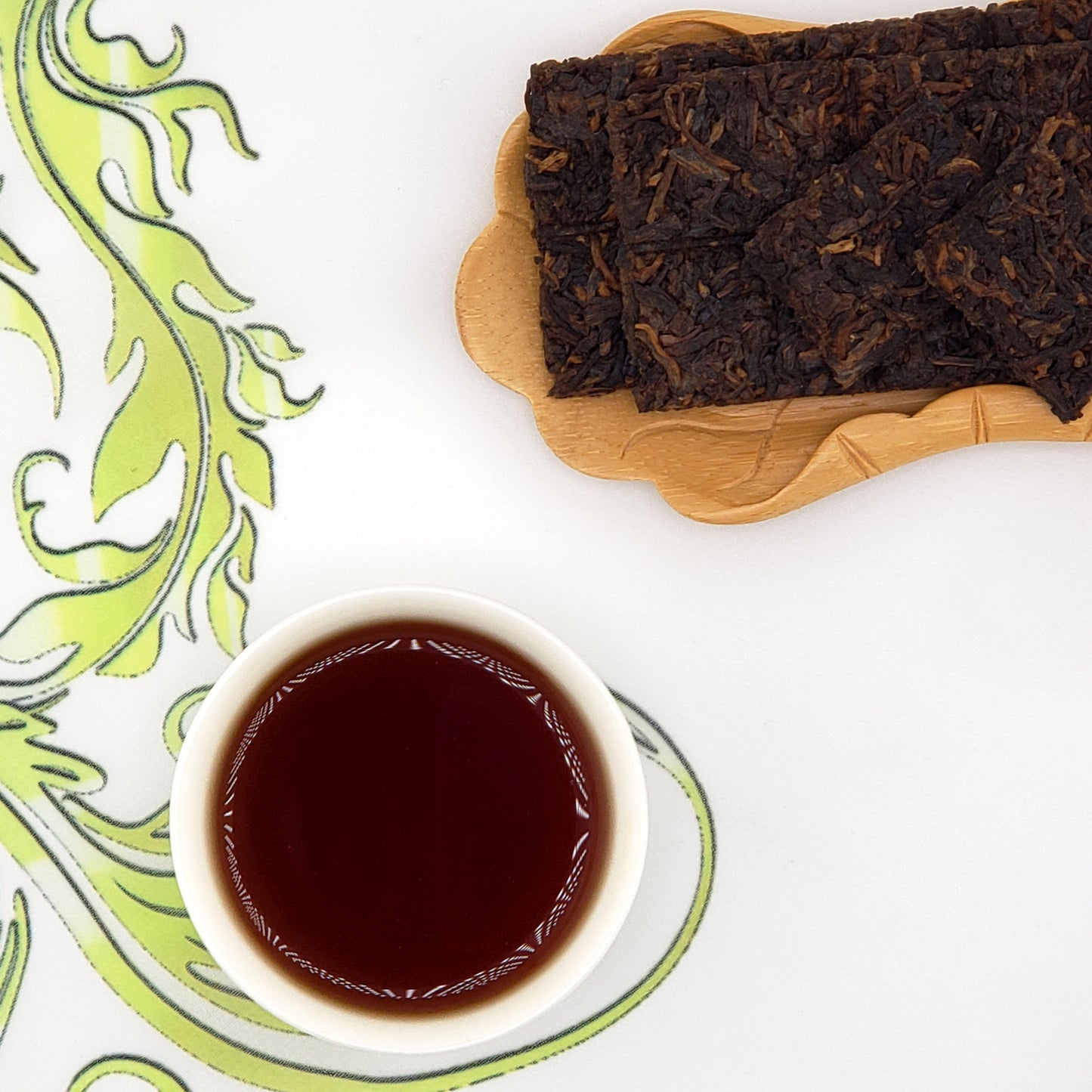 Puer tea bricks on a wooden board with a cup of tea on a decorative white and green plate.