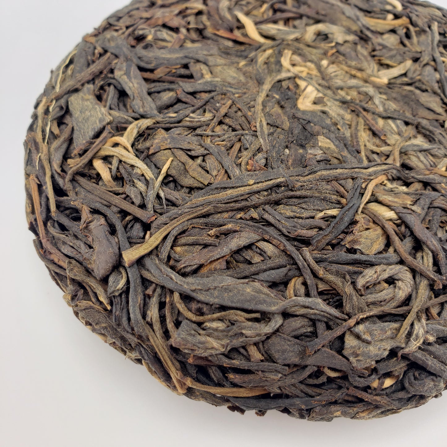 Close-up of a compressed tea cake with twisted tea leaves on a white background