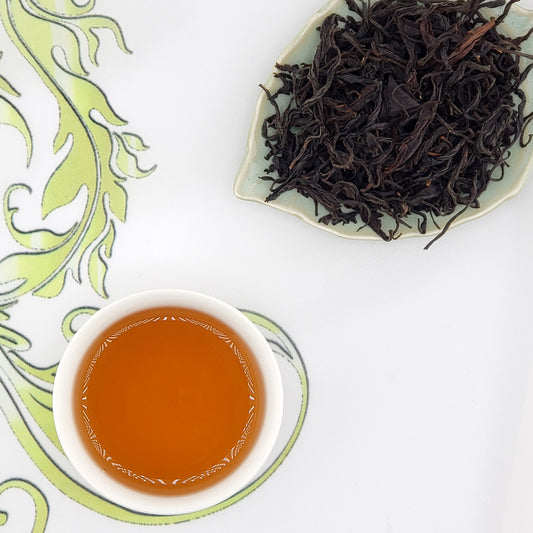 Dried black tea leaves on a leaf-shaped plate with a cup of brewed tea.