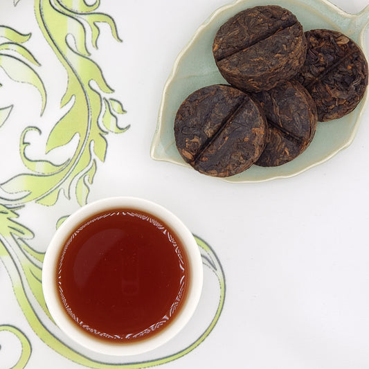 Pressed tea coins, scored down the middle, with a cup of tea on a decorative surface