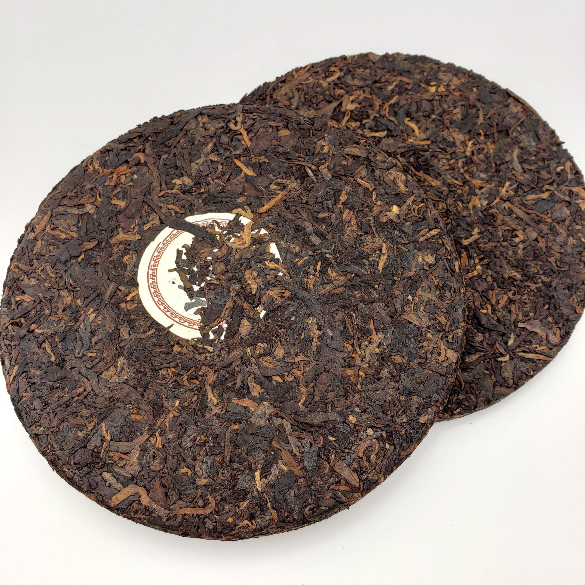 Two round dark brown tea cakes with a visible brand logo on a white background