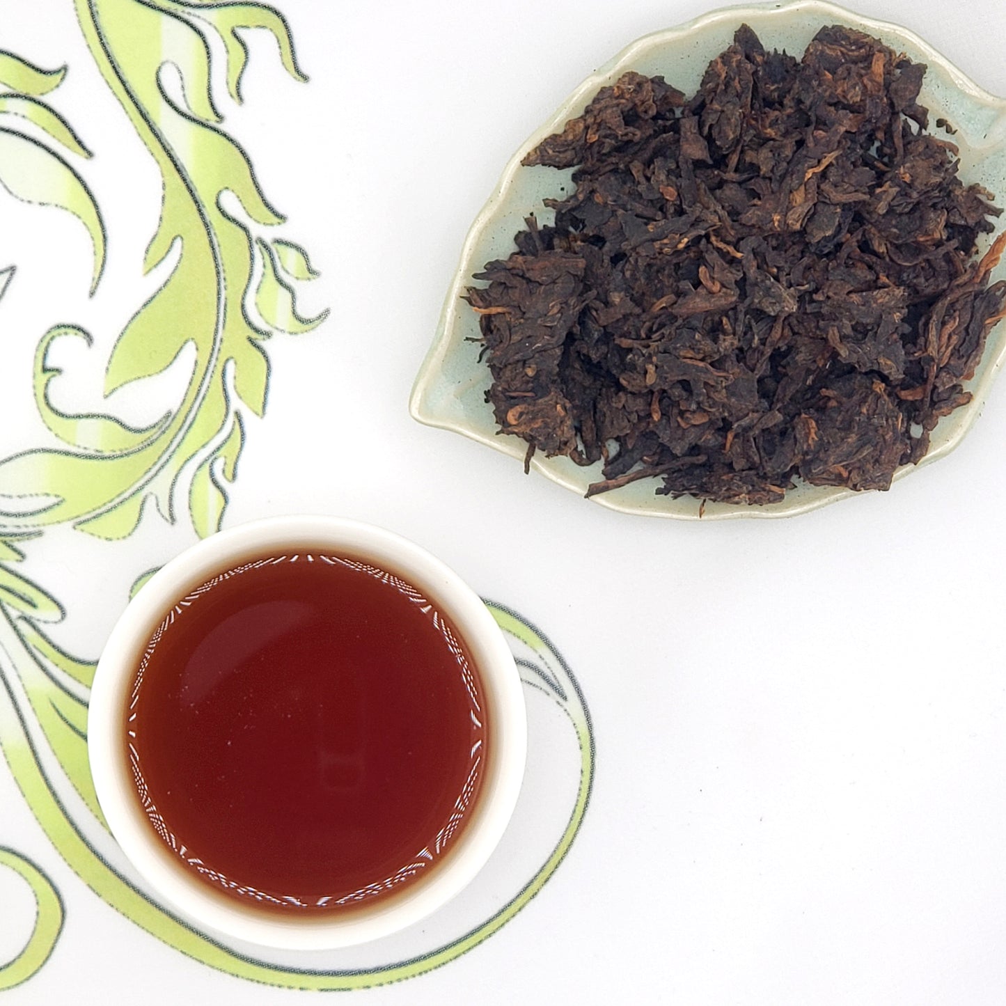 Pu-erh tea leaves broken from pressed cake and a cup of brewed tea, rich mahogany color.