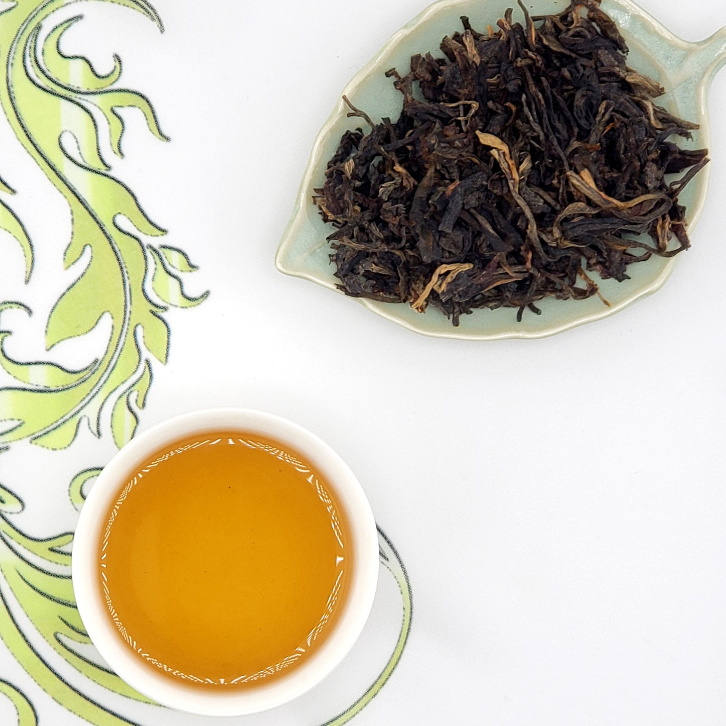 Tea cup with brewed tea and a dish of dry tea leaves on a decorative white background