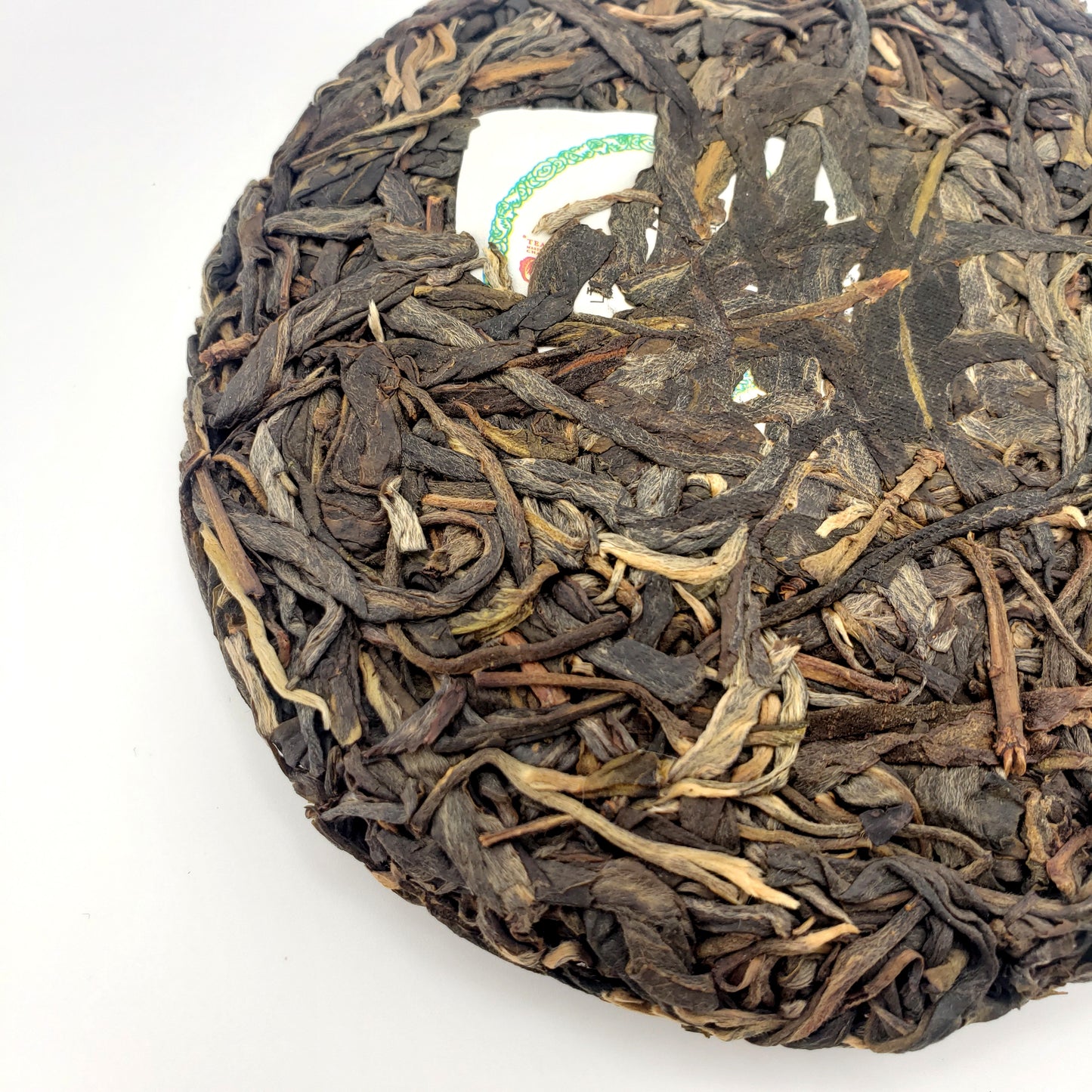 Close-up of a round, pressed tea cake with dried tea leaves on a white background